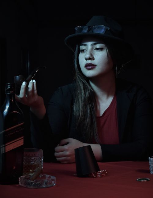 Free Elegant woman in hat, seated at a table with poker chips and drink, creating a moody casino atmosphere. Stock Photo
