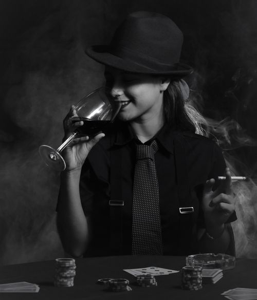 Free Elegant woman in monochrome sipping wine, holding cigarette, exuding a vintage, noir atmosphere. Stock Photo