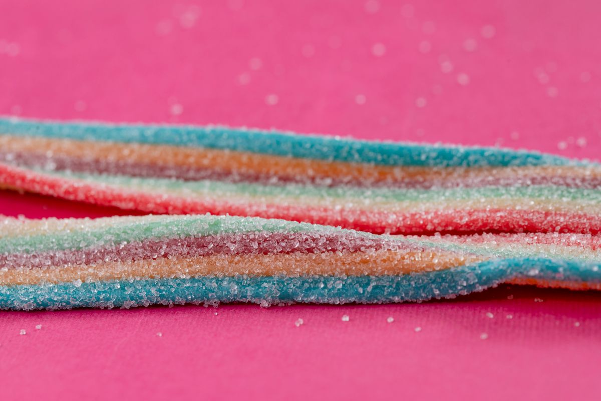 Close-up of rainbow-colored candy strips with sugar on a pink surface.