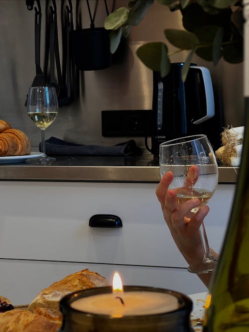 A Hand Holding a Glass of Wine Near Lighted Candle