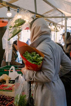 A woman in a coat shopping for fresh vegetables at an outdoor street market.