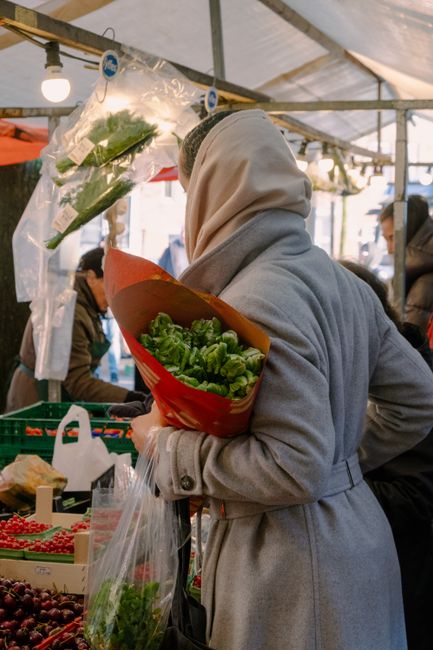 A woman in a coat shopping for fresh vegetables at an outdoor street market.