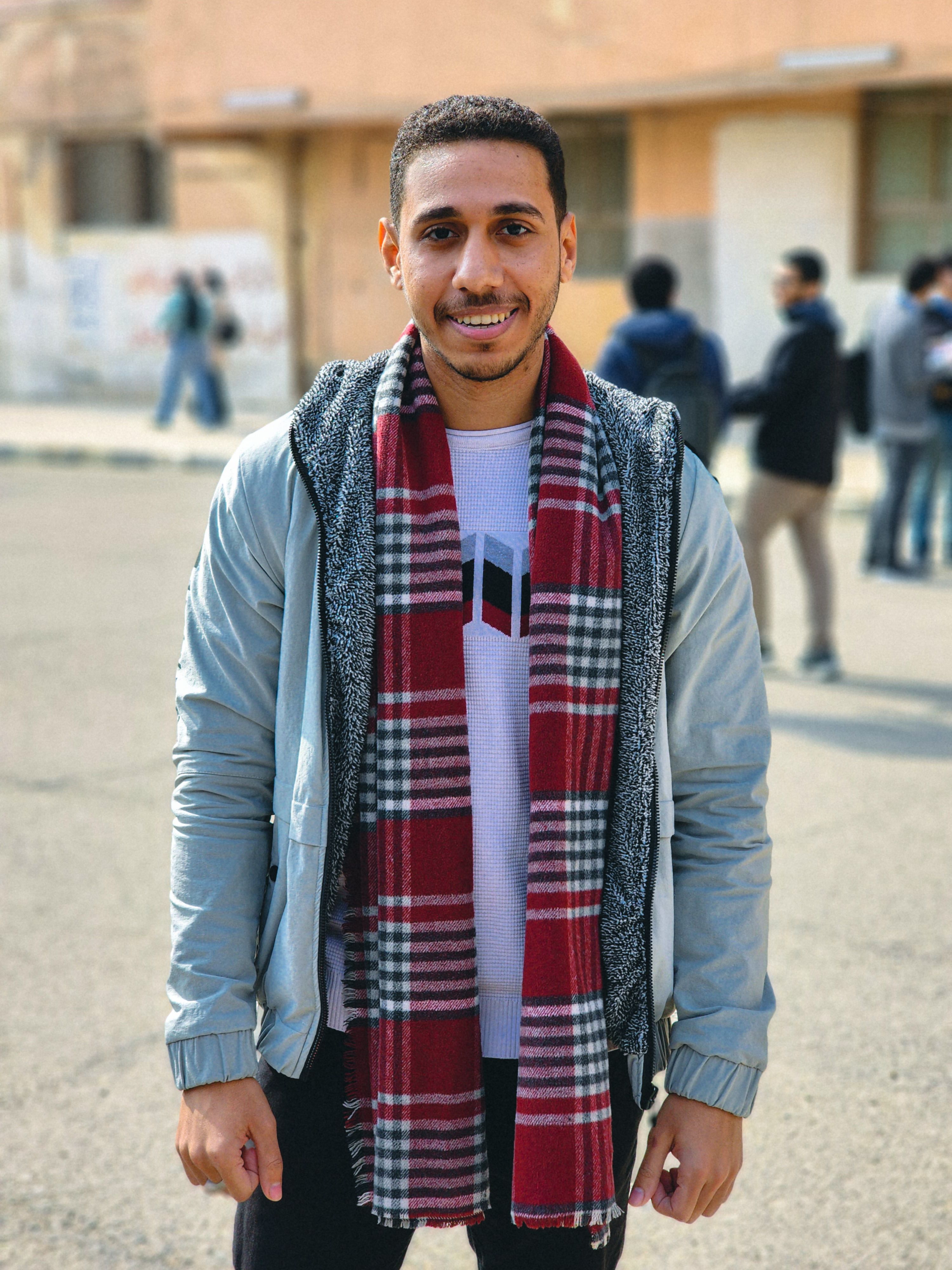 Portrait of a fashionable young man outdoors wearing a plaid scarf with a warm smile.