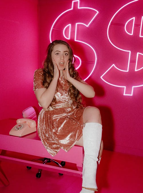 A Shocked Woman in Pink Dress Sitting on Wooden Table 