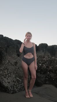 Fashionable woman in polka dot bikini standing on rocky beach during summer day.