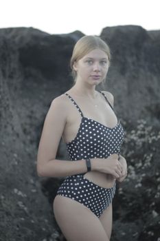 Stylish woman in polka dot swimsuit posing outdoors with rocky background.
