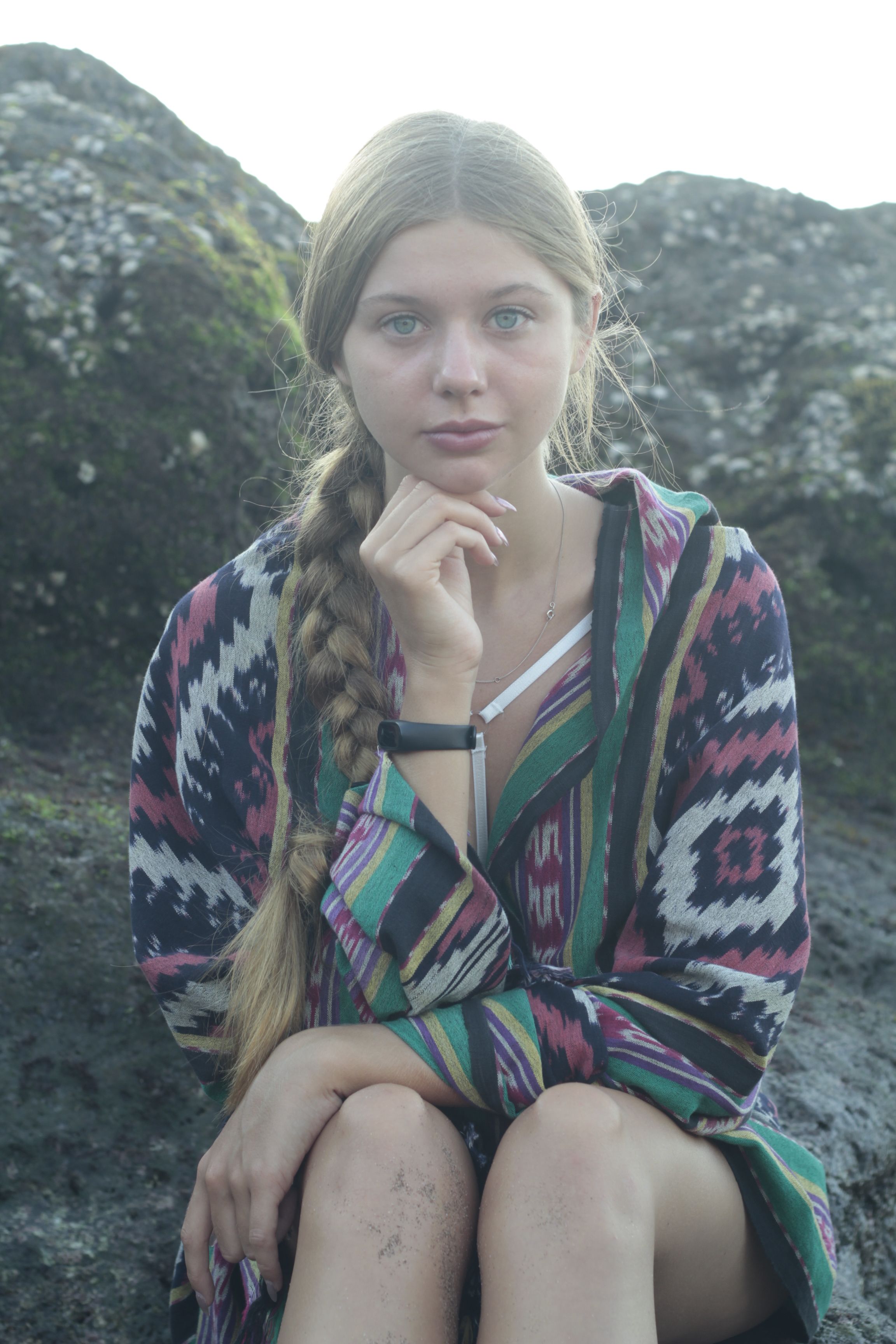 Young woman with a braid sitting on rocks in a colorful poncho.
