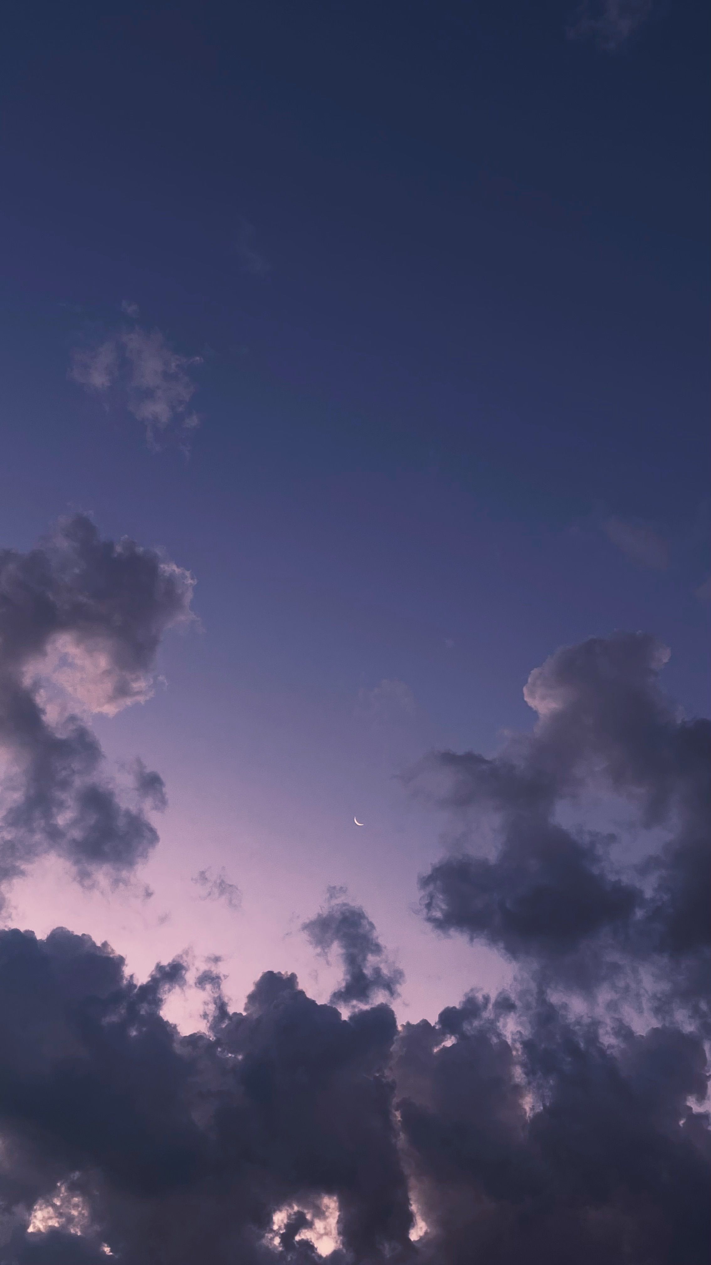 A tranquil twilight sky featuring a crescent moon surrounded by clouds, creating a peaceful atmosphere.