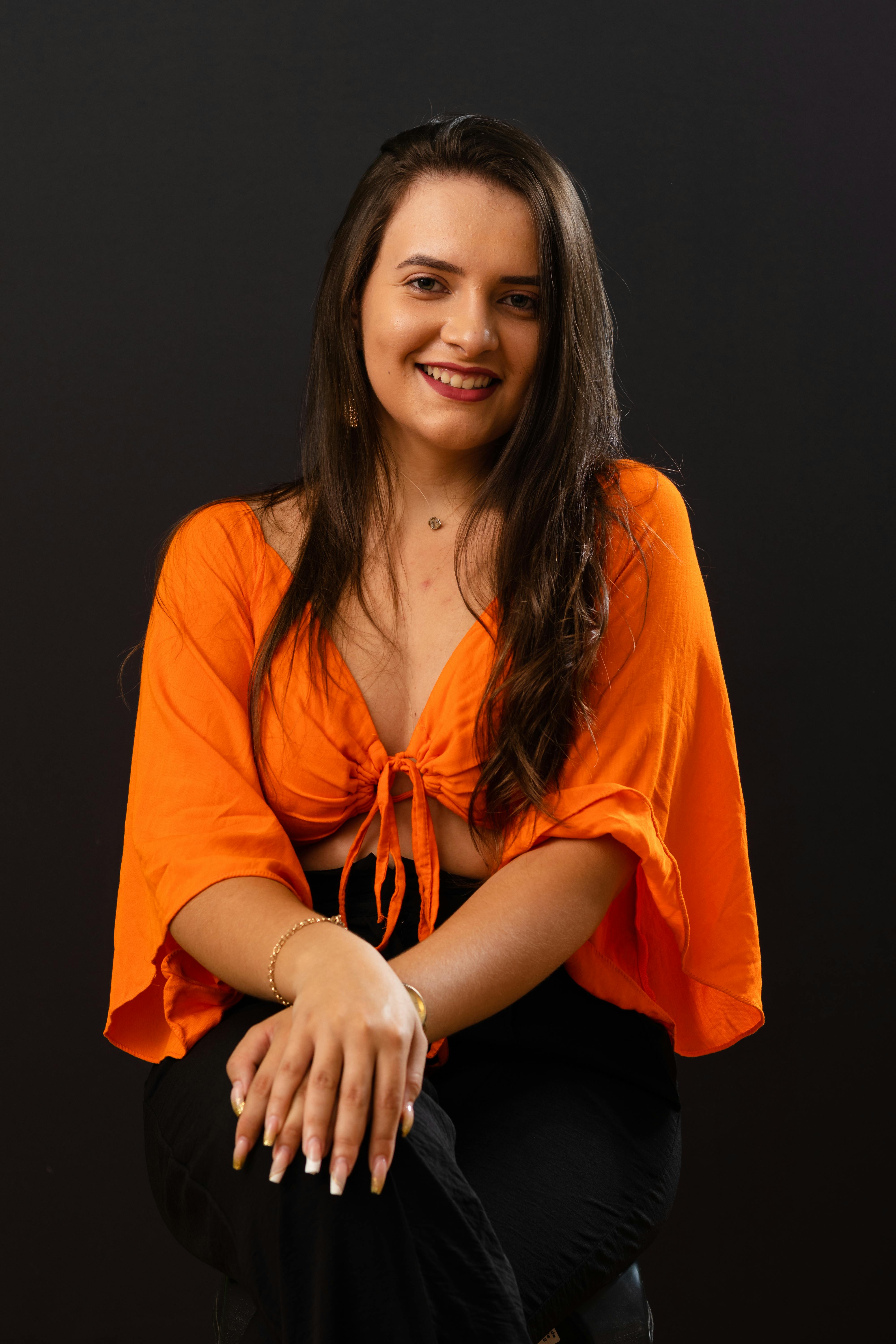 Charming portrait of a woman in orange attire smiling against a black background.