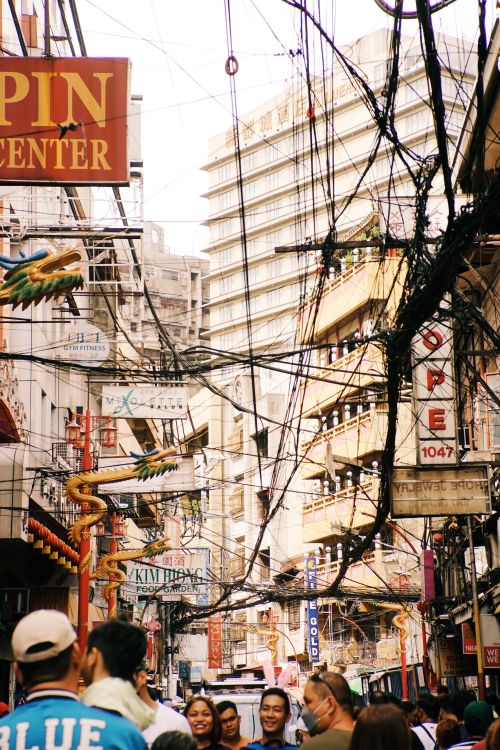 Free Busy city street scene with tangled overhead cables and vibrant signs, capturing urban life. Stock Photo