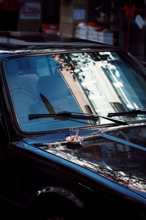 Free A Turkish tea glass rests on a car hood, reflecting an urban street scene in Türkiye. Stock Photo