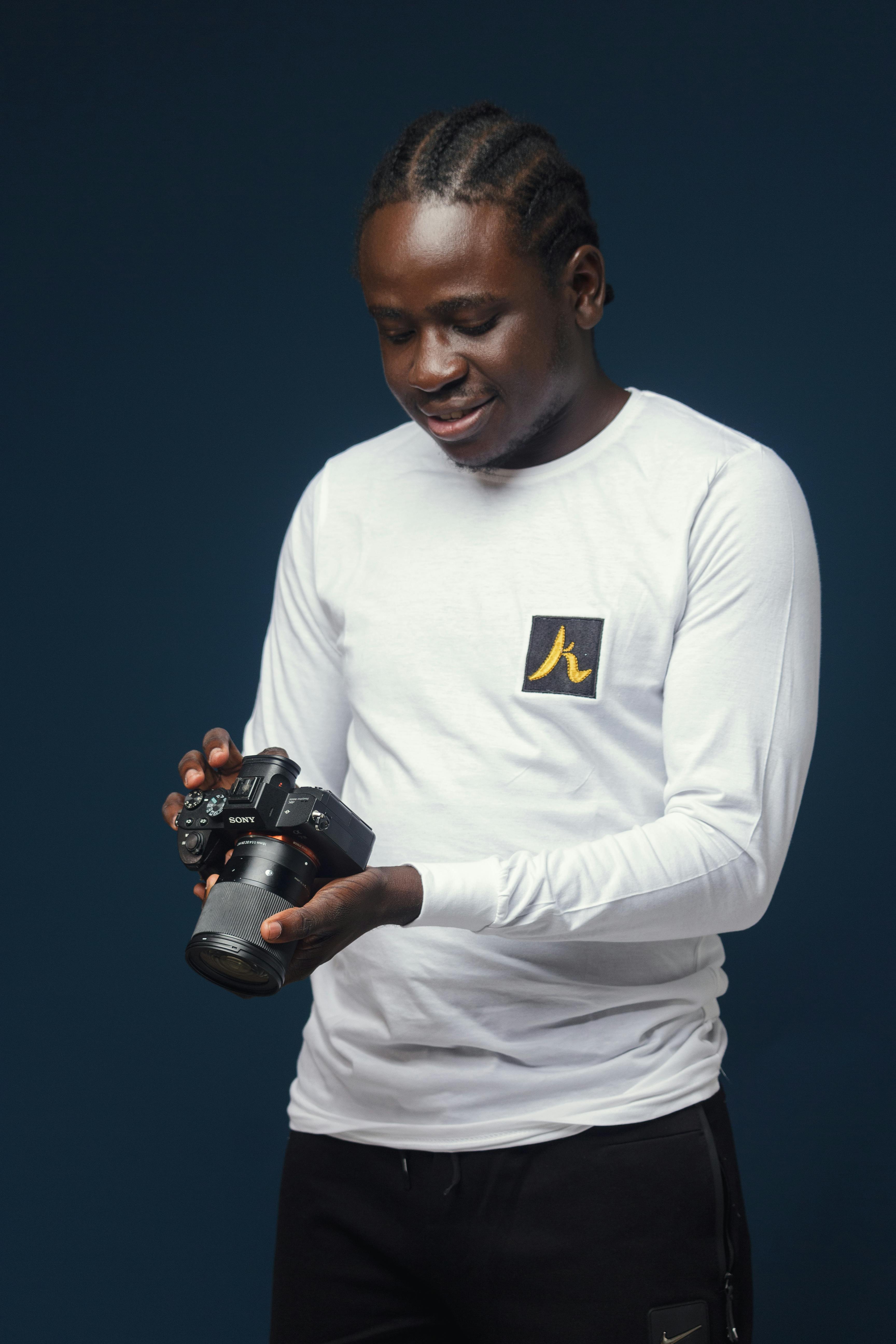 Studio shot of a smiling photographer holding a camera against a dark background.