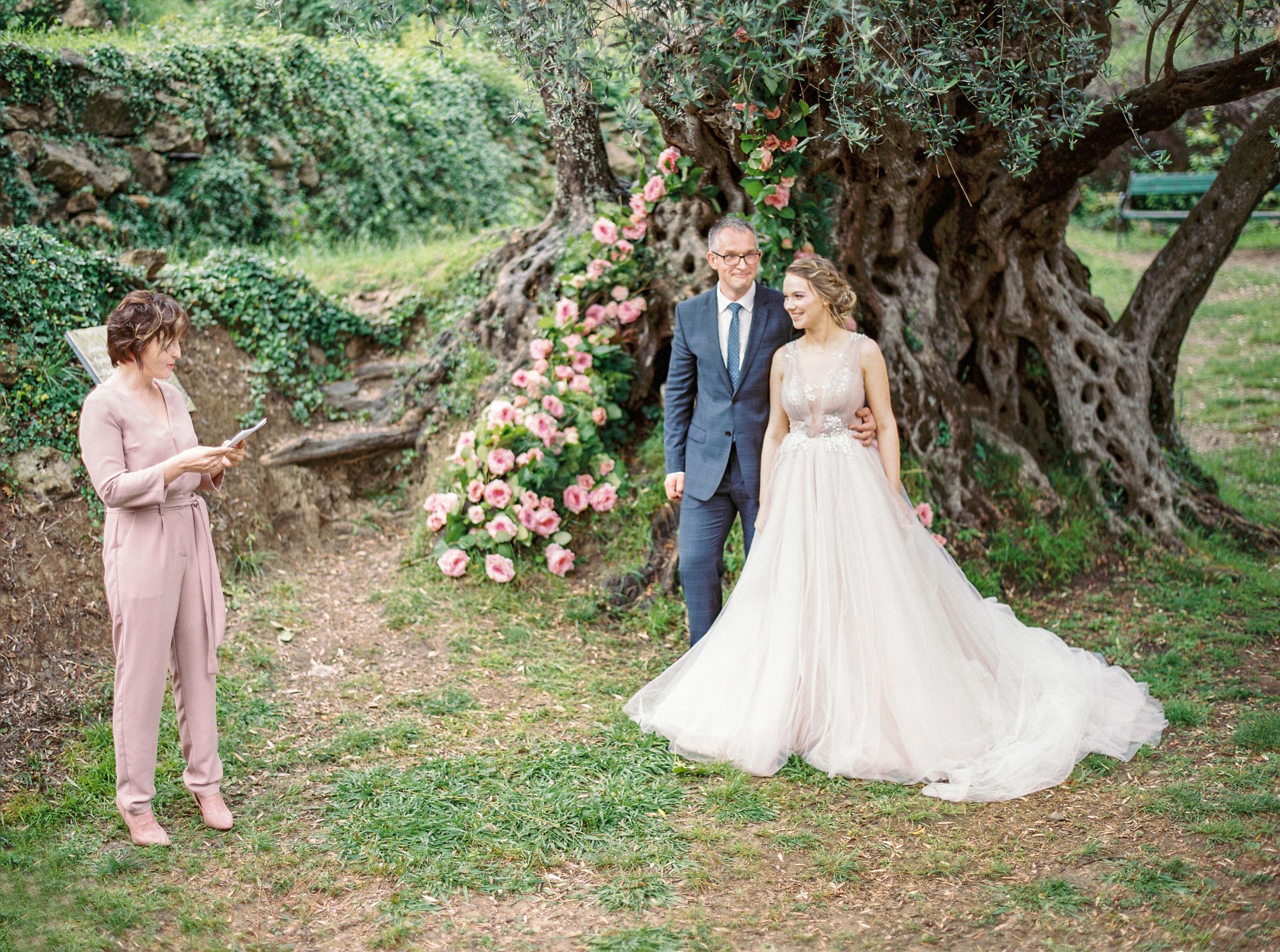 Newlyweds pose under a tree with floral decor during a wedding ceremony.