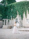 一位令人惊叹的新娘在一座常春藤覆盖的石头建筑城堡旁边穿着优雅的婚纱