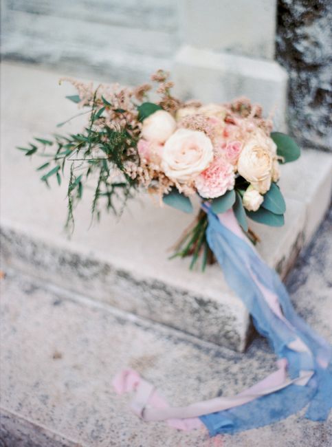 A romantic bouquet of roses with a blue ribbon, placed on a rustic stone staircase, perfect for weddings.