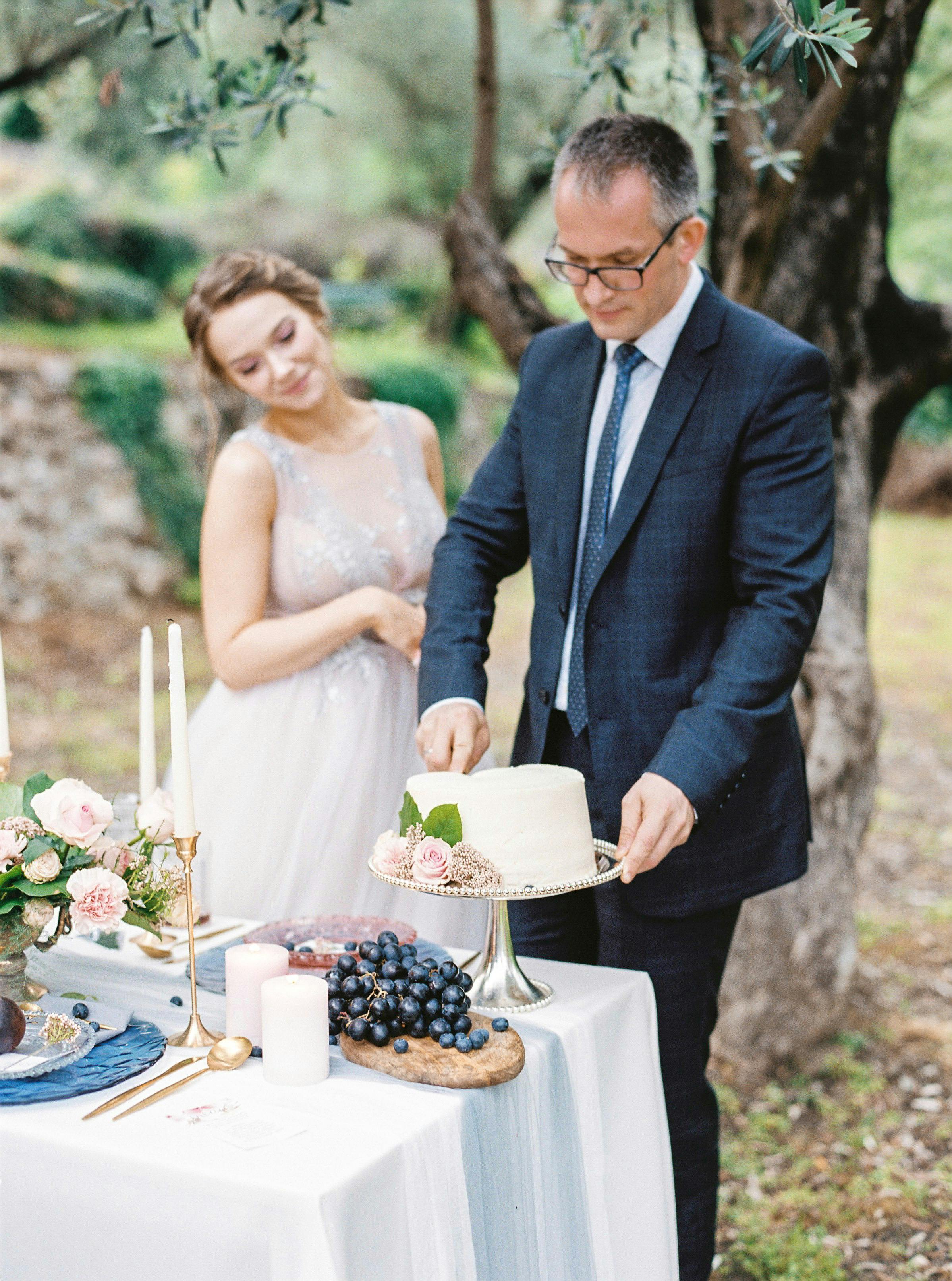 Newlyweds cutting a wedding cake at a beautiful outdoor setting adorned with flowers and candles.