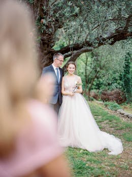 Romantic newlyweds portrait in elegant attire under a lush tree outdoors.