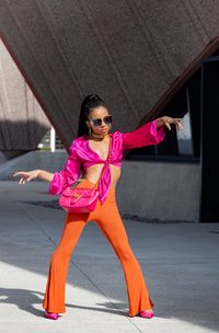 Woman in pink and orange against concrete architecture — photo by PeopleByOwen on Pexels