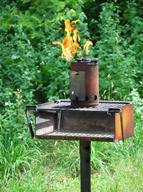 Free Close-up of an outdoor grill with a chimney starter igniting flames in a lush green setting. Stock Photo