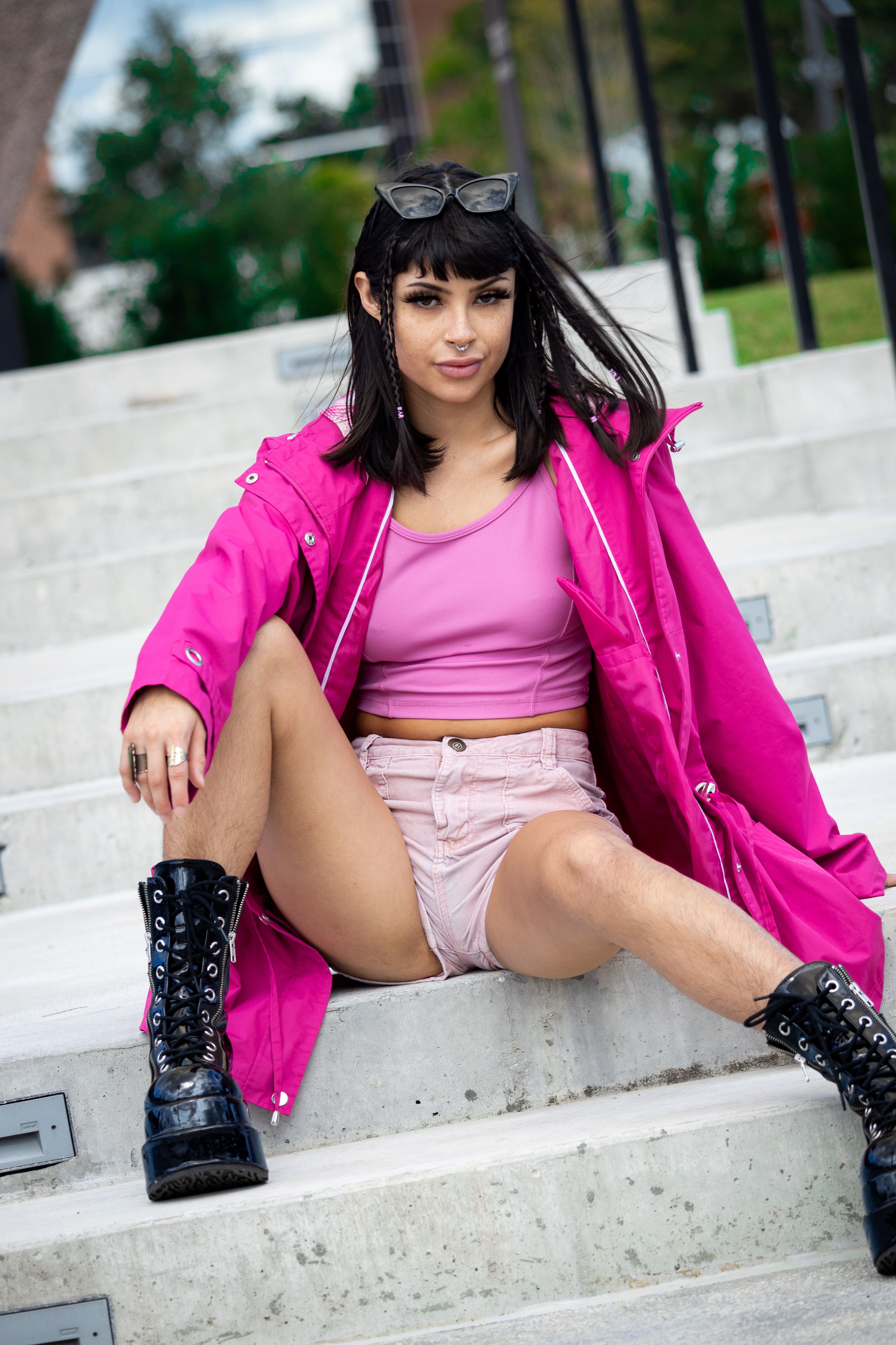 Confident fashion model sitting on concrete steps in a vibrant pink coat, exuding modern style and boldness.