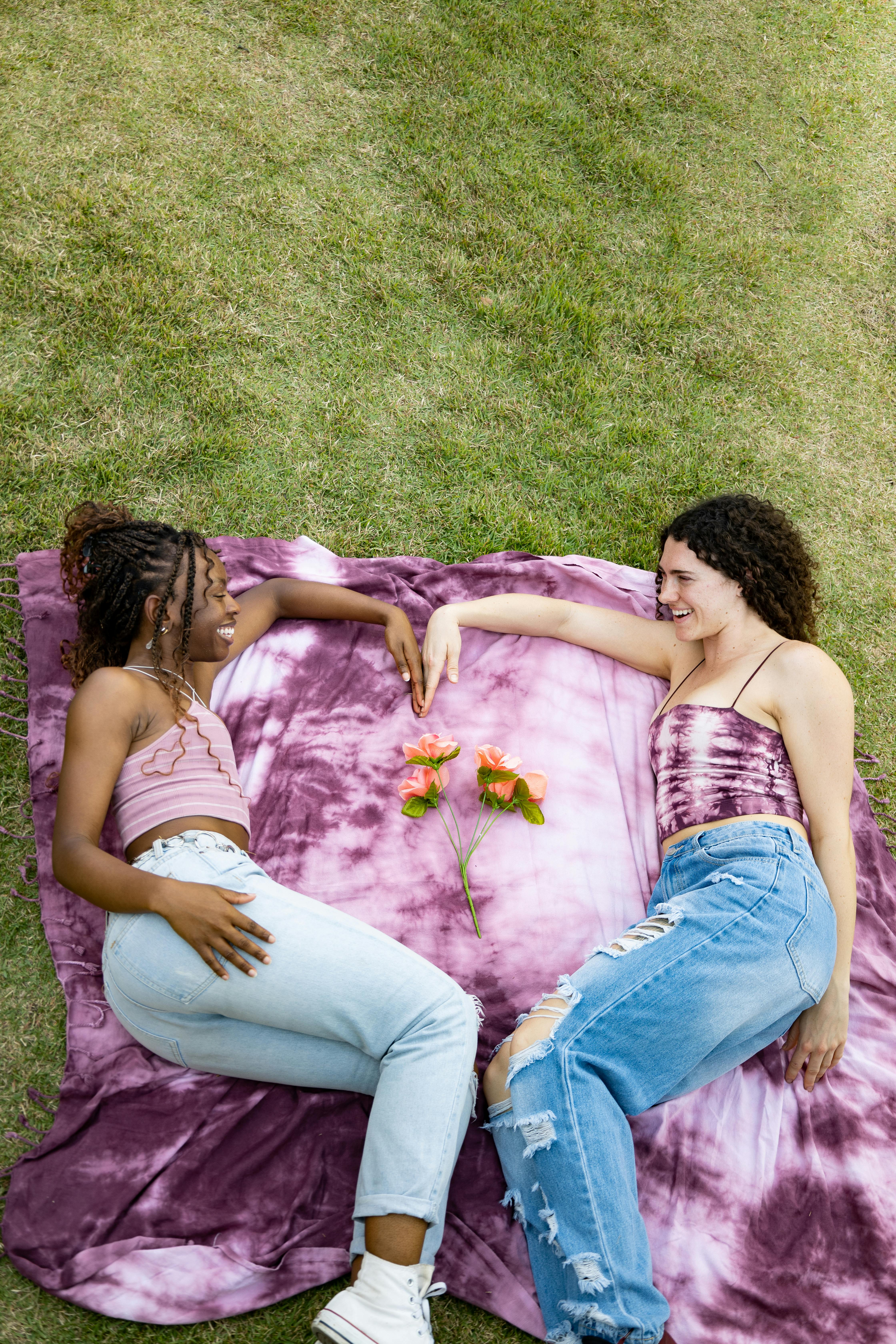 women lying on the blanket with a flower between them