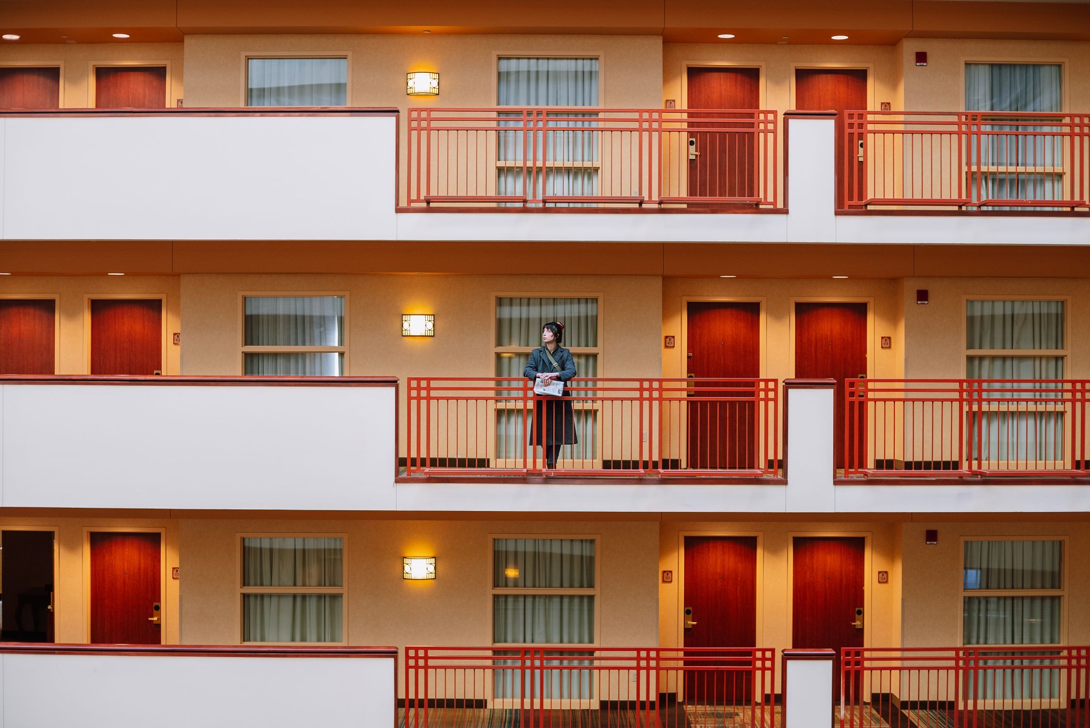 Man standing on balcony of a modern residential building, displaying symmetry and architecture.