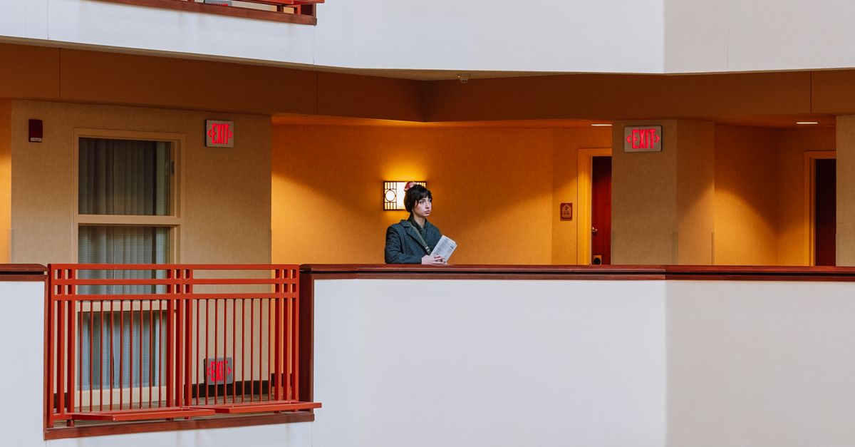A woman standing in a modern hotel corridor with balconies and red railings.
