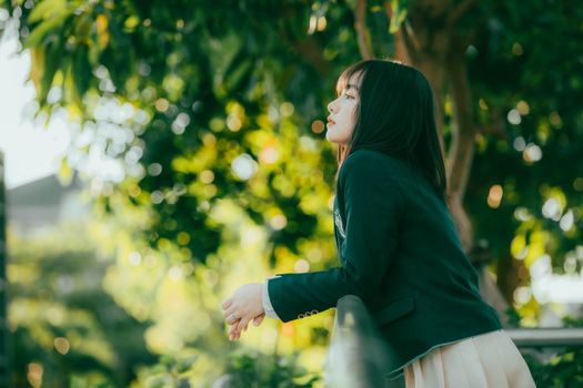 A young woman in a green blazer enjoys the serene atmosphere of a sunlit park.