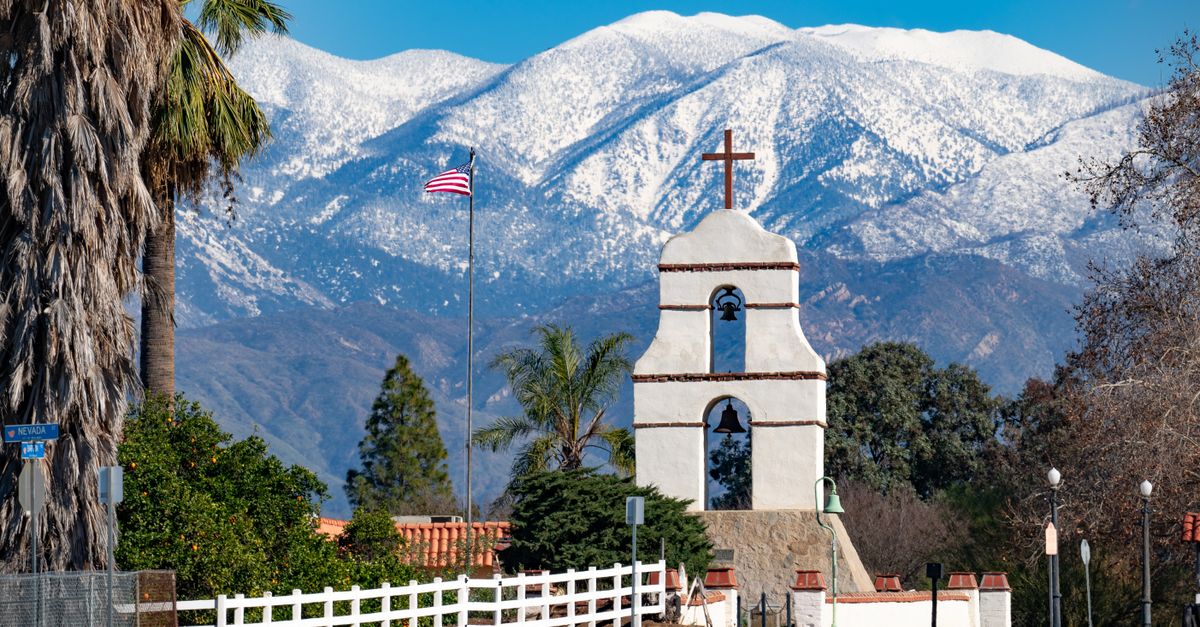 Bell tower and American flag against snowy mountains in a sunny winter landscape.