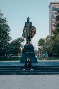 A man sitting on steps in front of the Cuauhtémoc statue in Toluca de Lerdo, Mexico.