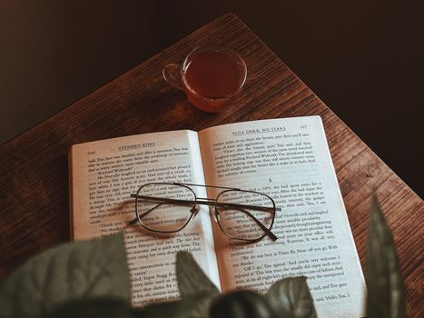 Warm and inviting scene of a book, glasses, and tea on a wooden table, perfect for readers.