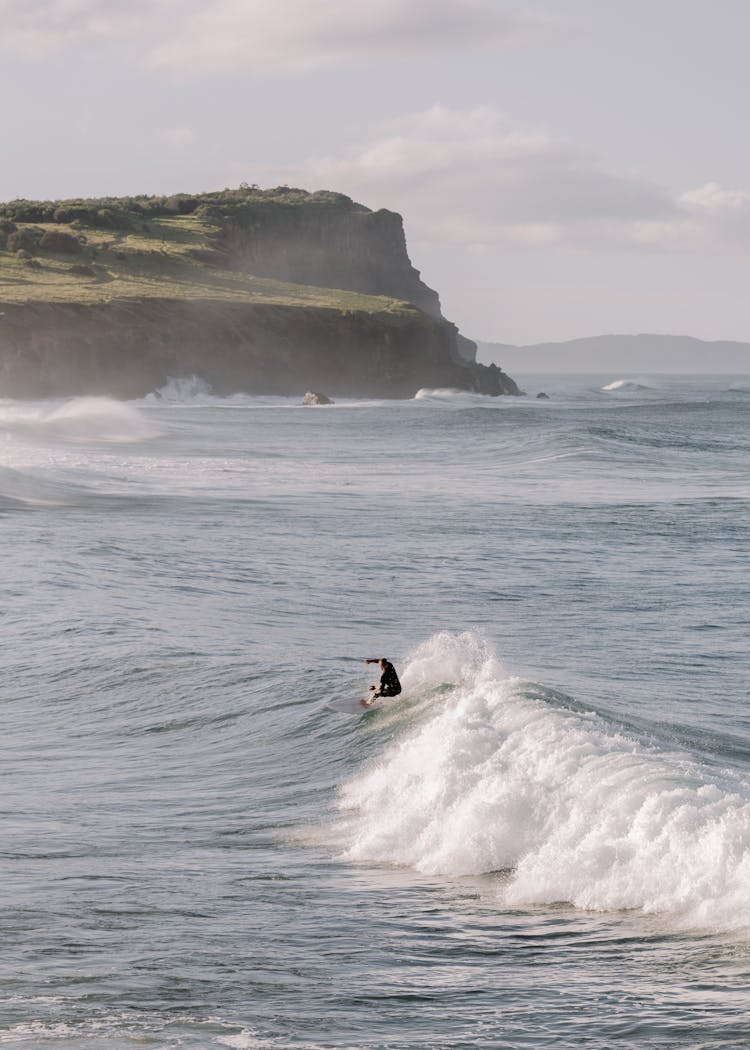 Surfer On Wave Near Sea Shore With Cliff