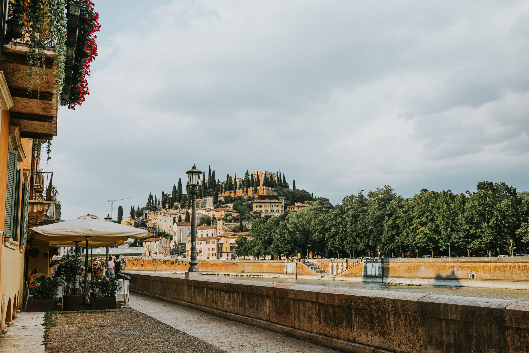 Explore the picturesque riverside promenade in Verona with lush greenery and historic architecture.