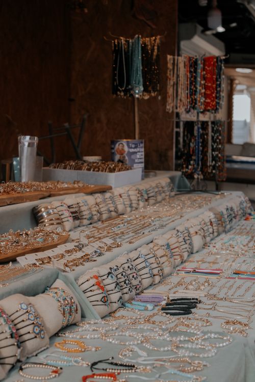 Free An array of handcrafted bracelets, necklaces, and jewelry displayed on tables in a market setting. Stock Photo
