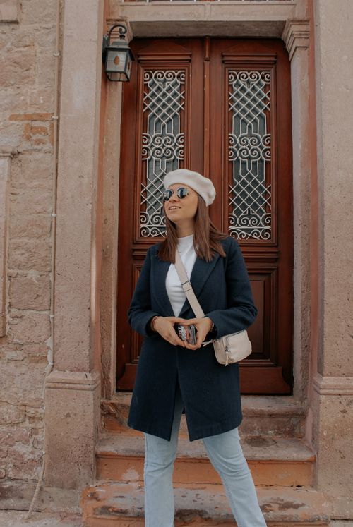 Free Stylish woman in a coat and beret poses confidently by a decorative door. Stock Photo