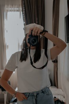 A young woman uses a DSLR camera to capture a mirror selfie in a stylish room.
