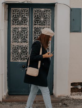 A fashionable woman in denim jeans and black blazer walks past a vintage door, adding urban charm to her stride.