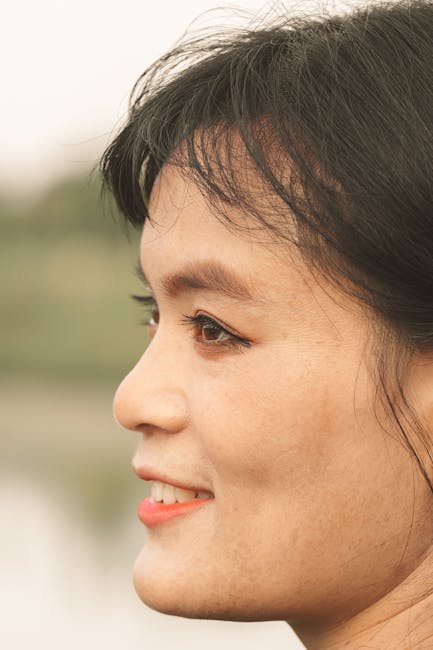 Close-up side view of a woman smiling against a blurred outdoor background.