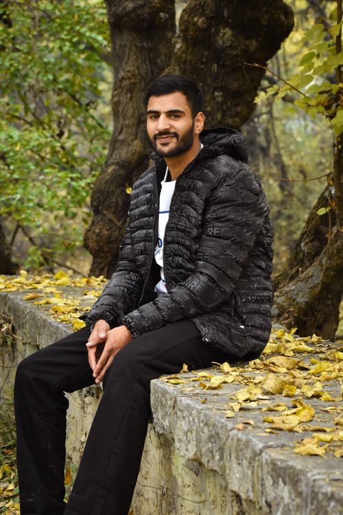 Free Young man seated on stone wall in autumn park, surrounded by fallen leaves and trees. Stock Photo