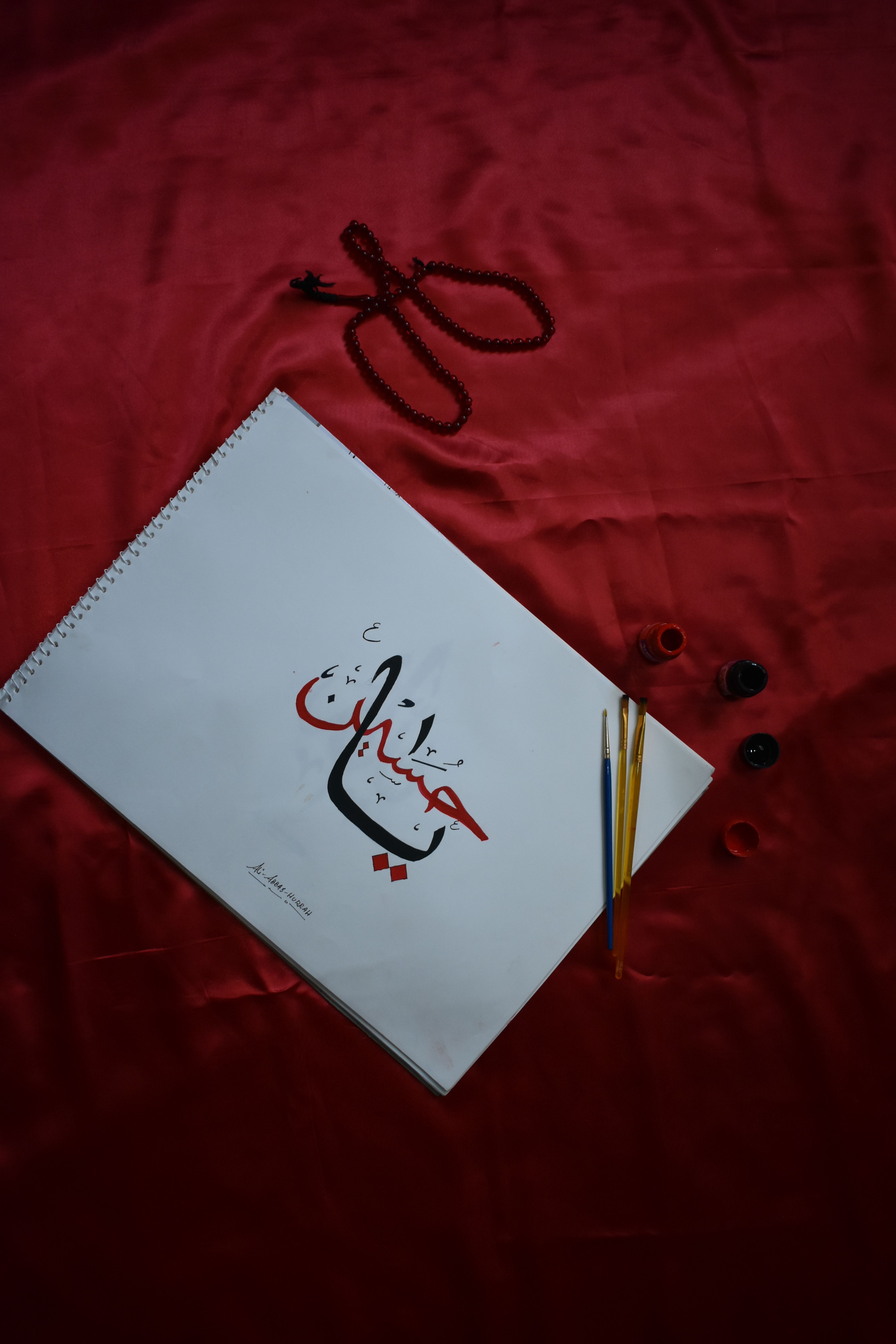 Close-up of Arabic calligraphy art with brushes on a red fabric canvas.