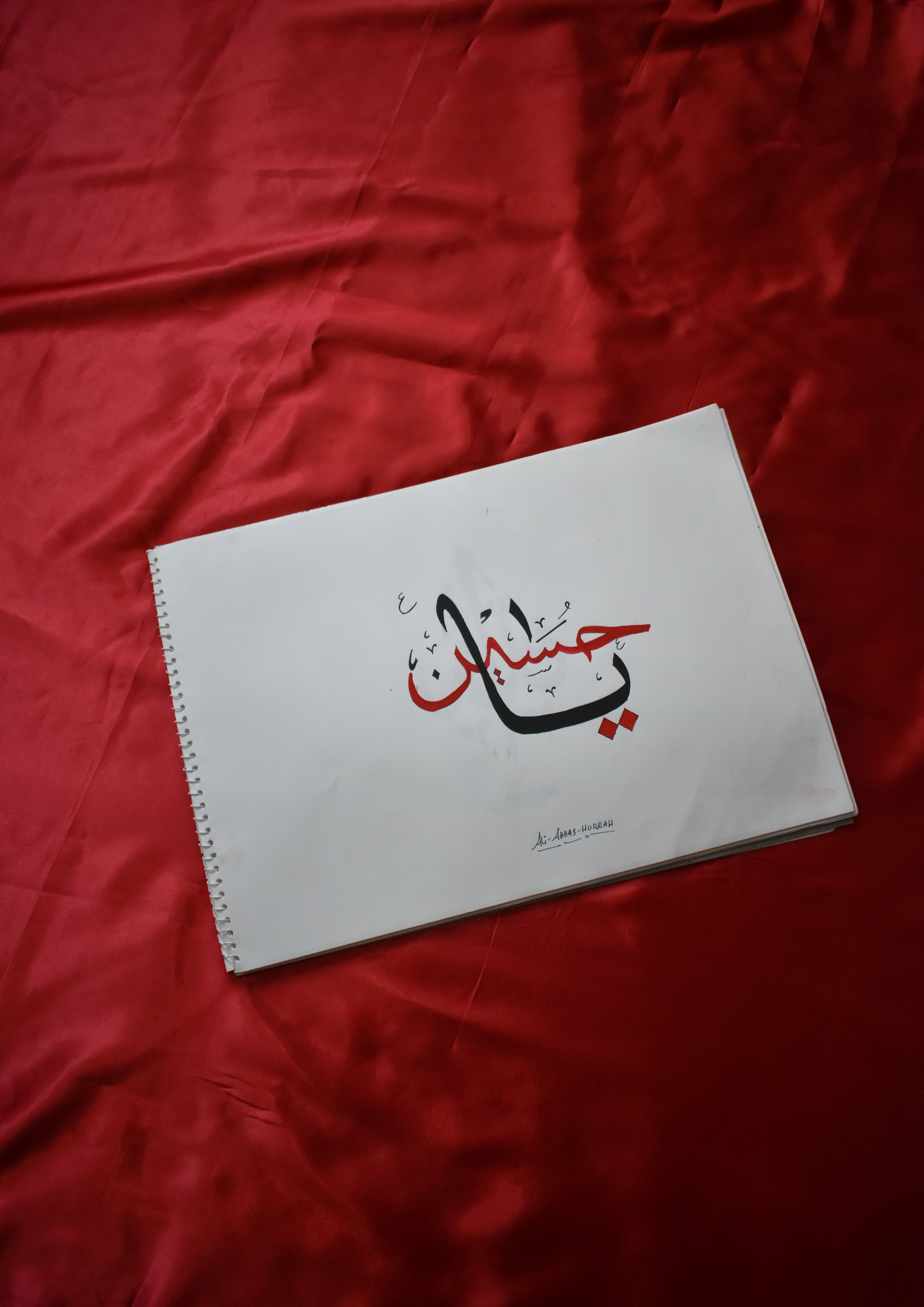 High-angle view of spiral notebook with Arabic calligraphy on red satin background.