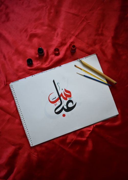 Free Elegant Arabic calligraphy on paper with ink pots and brushes on a red fabric background. Stock Photo