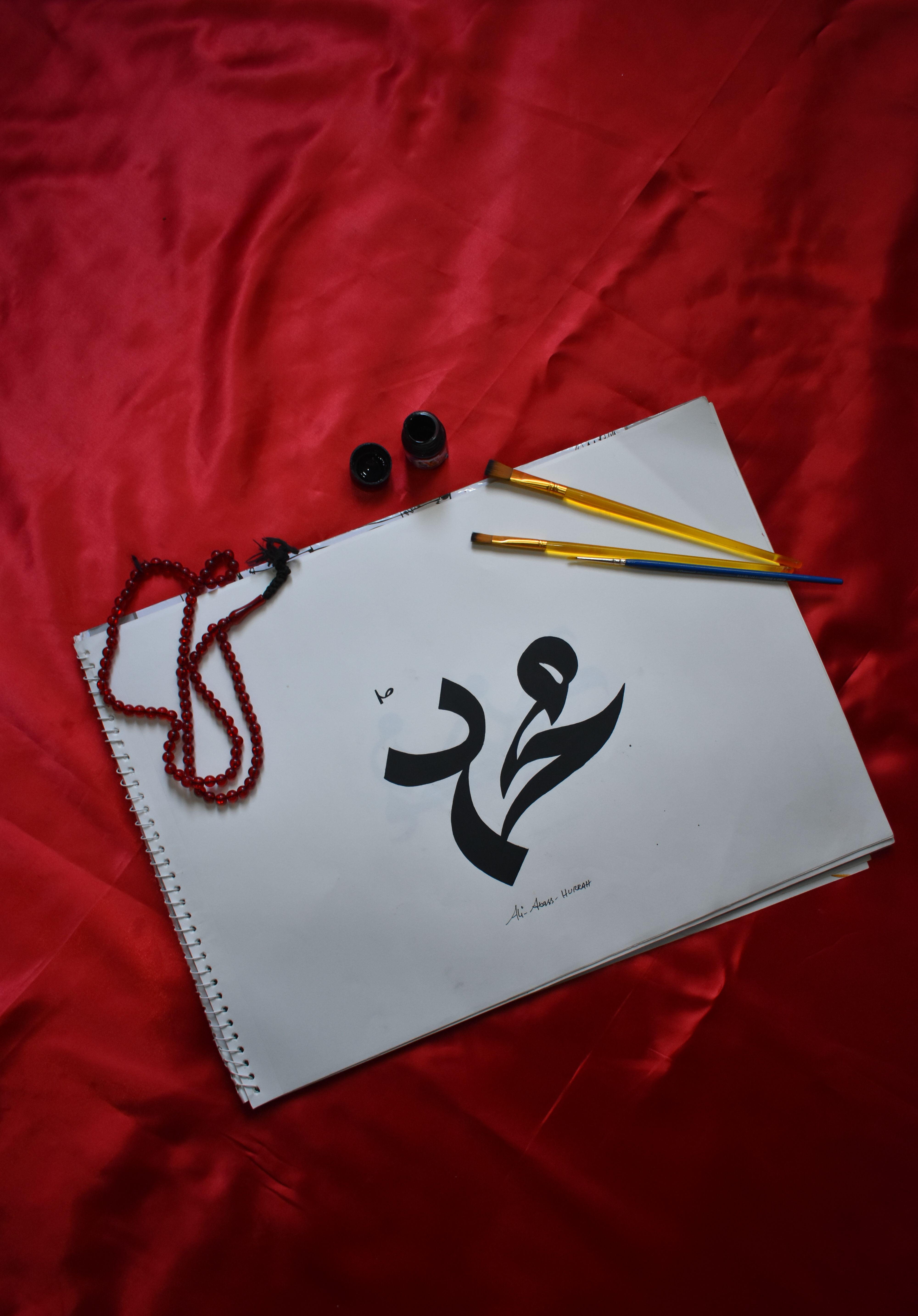 Sketchpad featuring Arabic calligraphy with paintbrushes on vibrant red background.