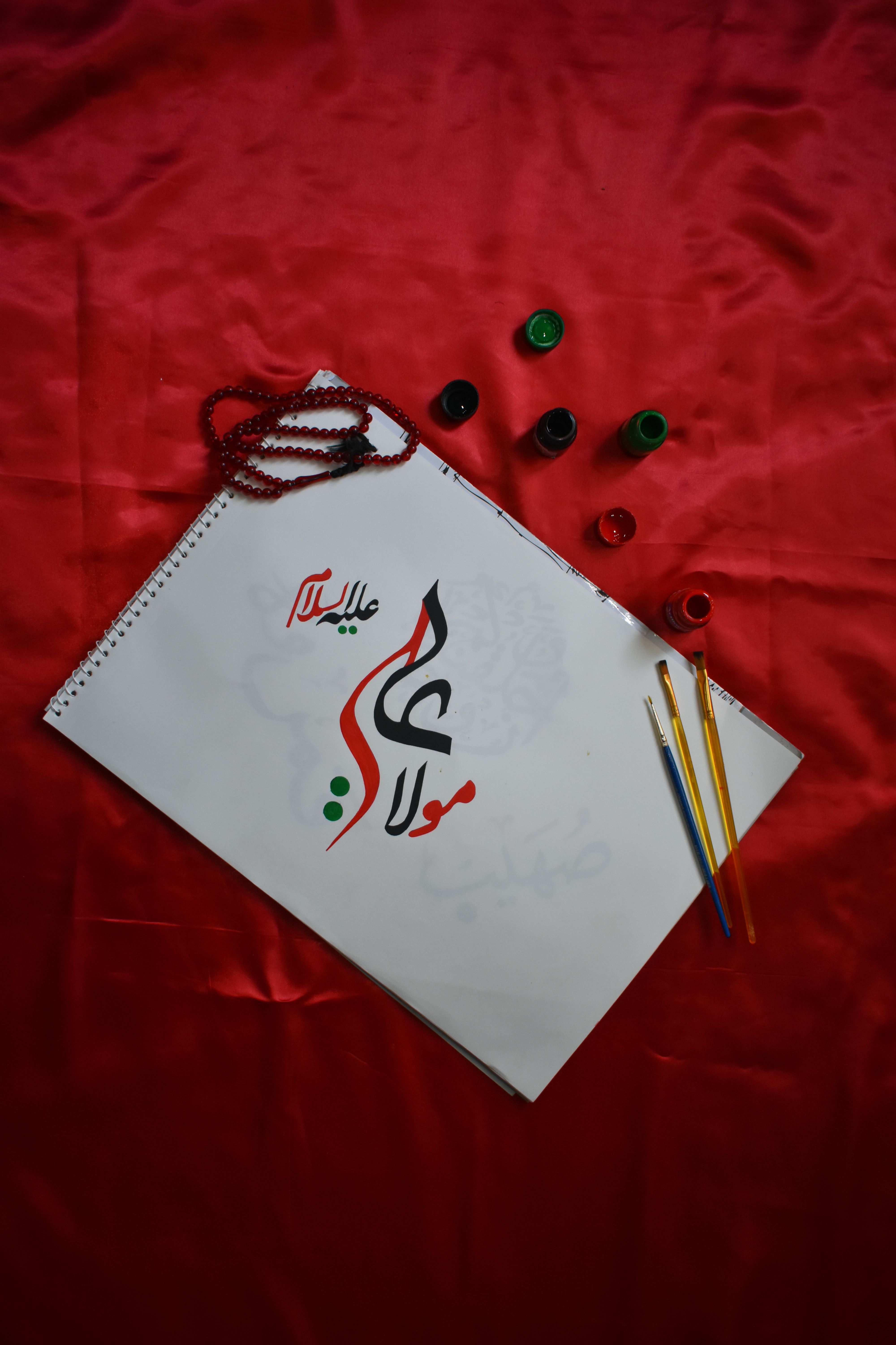 Artistic Arabic calligraphy with paintbrushes and beads on a vibrant red background.