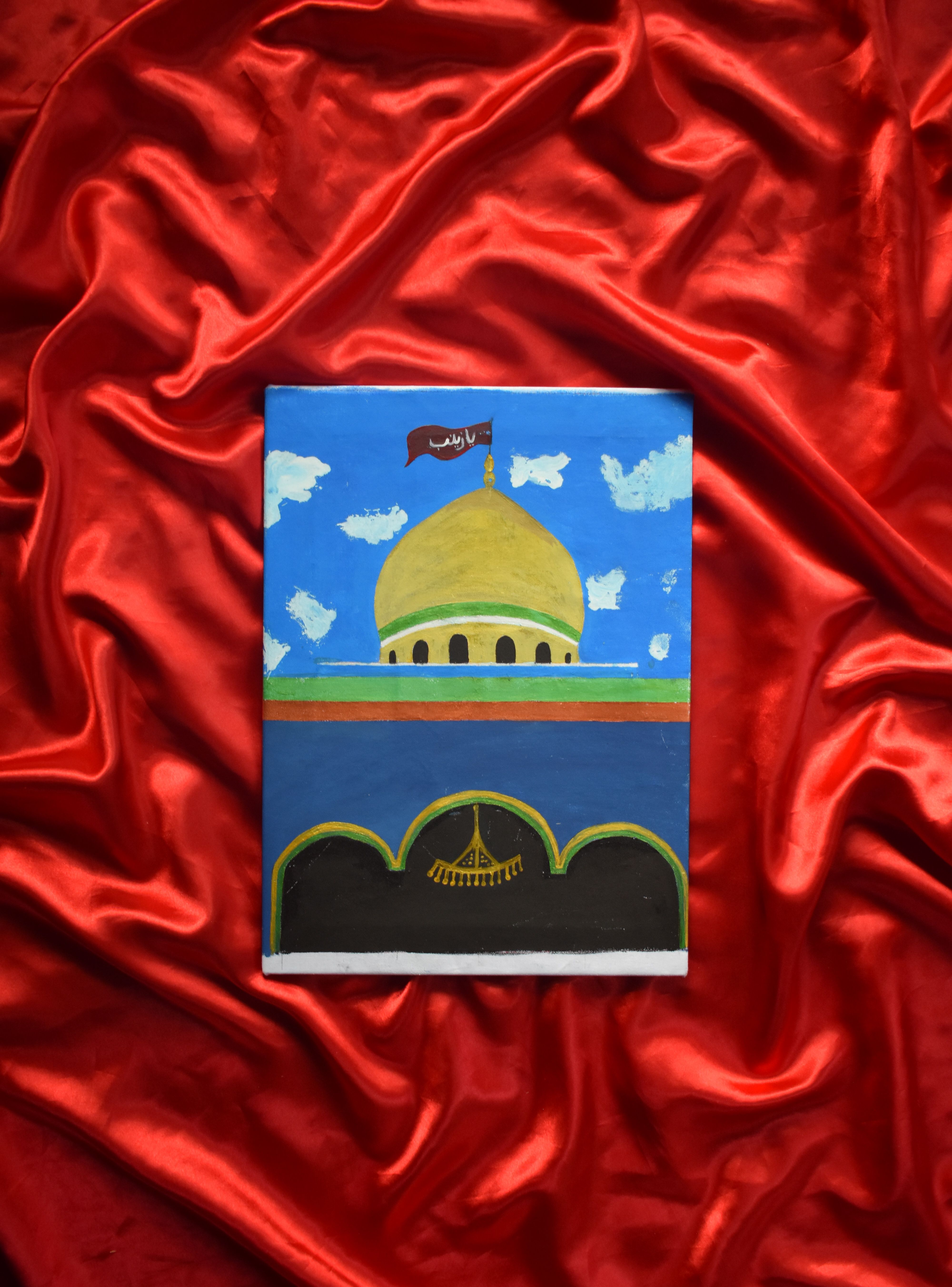 A colorful mosque painting displayed on luxurious red satin fabric.