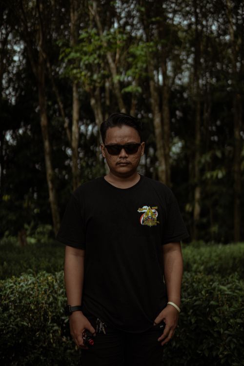 Free Man wearing black t-shirt and sunglasses stands amid lush trees in a summer park setting. Stock Photo