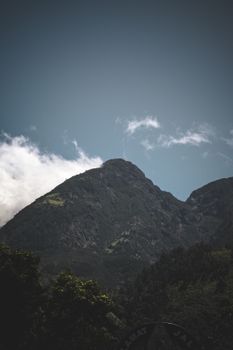 A stunning mountain peak rises into a clear blue sky with lush greenery at the base, showcasing natural beauty and tranquility.