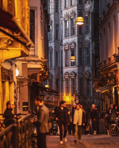 Free Beautiful evening scene with people walking through a historic urban alley, under warm street lights. Stock Photo
