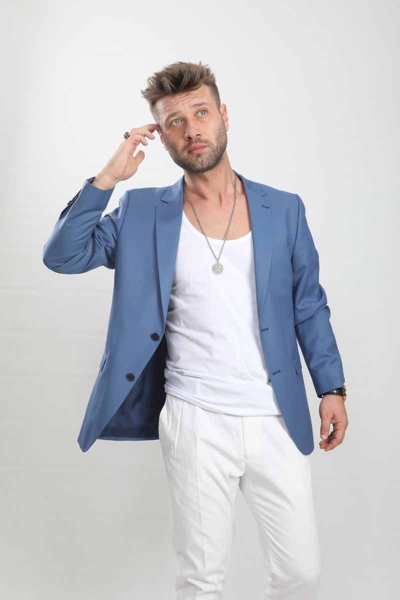 A man wearing a blue blazer over a white top and white trousers