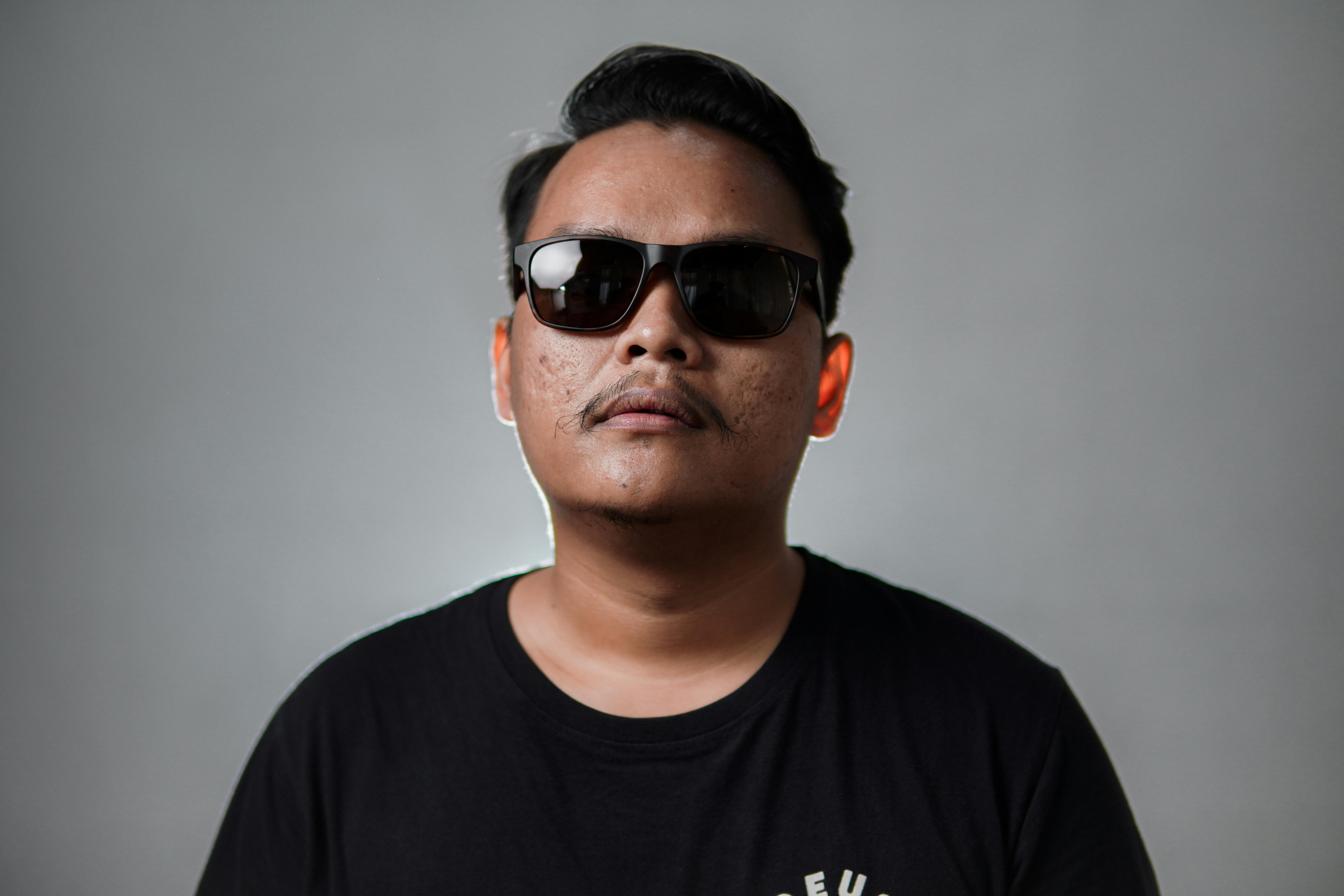 Portrait of a stylish man with sunglasses against a gray background, exuding a cool vibe.